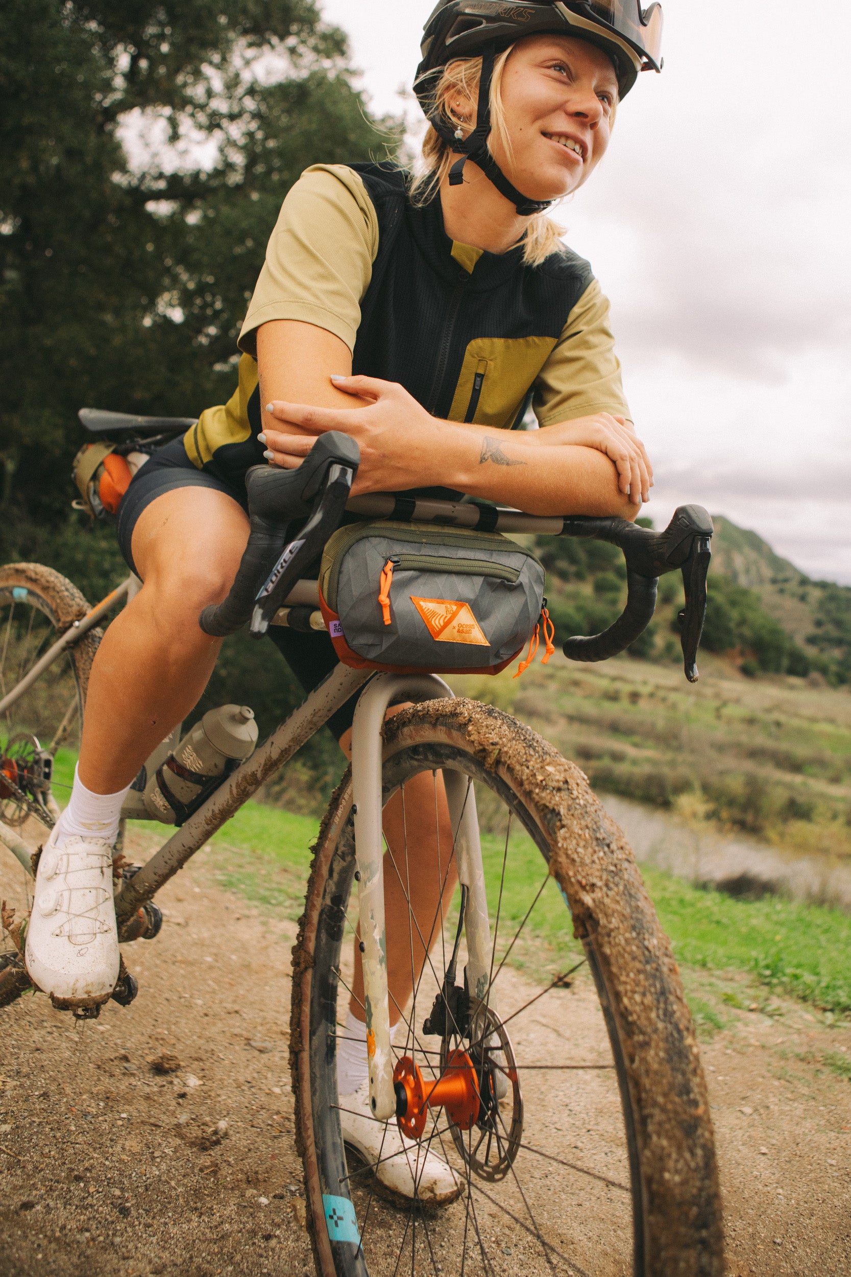 Person sitting on a bicycle with a bag, surrounded by nature