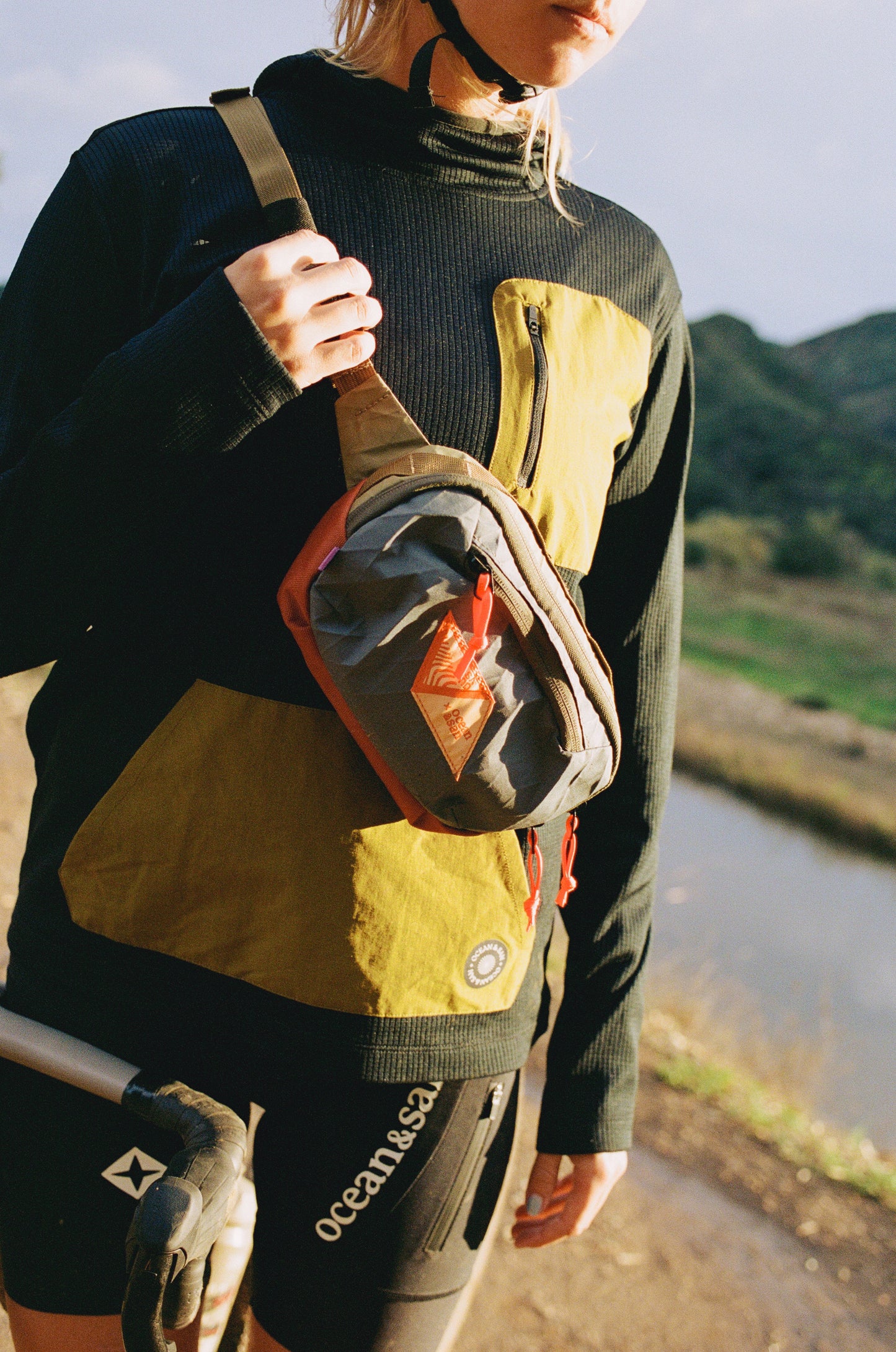 Person holding a crossbody sling bag with a scenic background